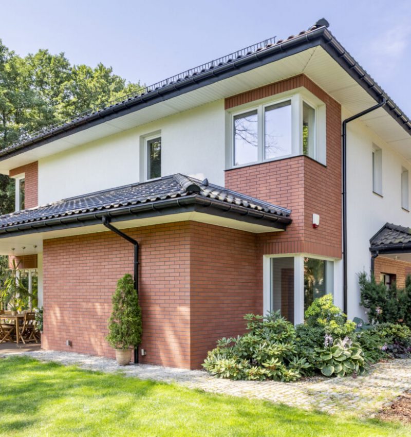 Red brick house with terrace and green grass and trees during summer